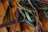 pile of handwoven bands and a backstrap rigid heddle